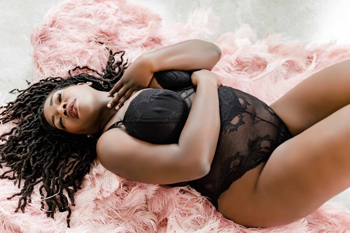 Dark skinned woman in dreadlocks laying on pink ostrich feathers
