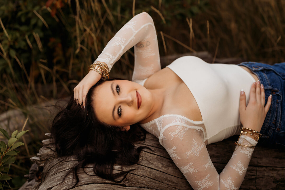 high school senior girl lays on a fallen tree stump just outside of Denver for her senior photos