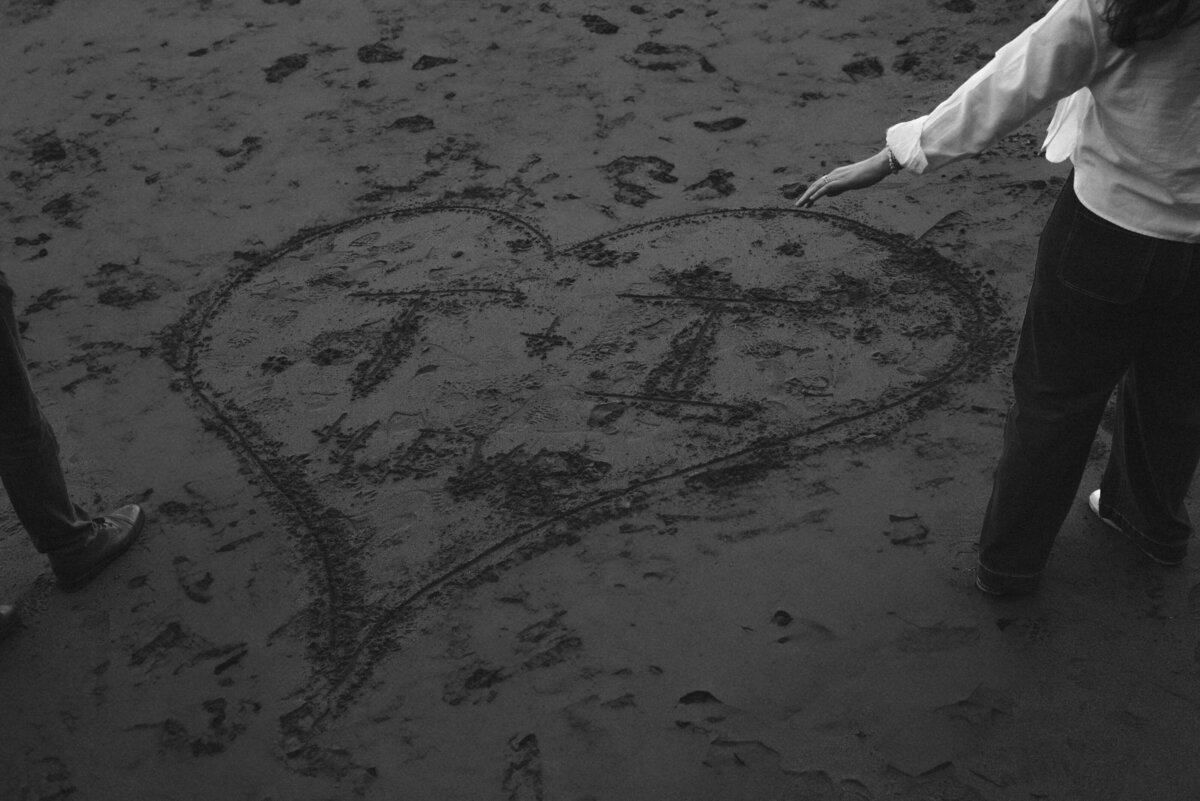 engagement session on the Oregon coast with drawing their initials in the sand during sunset
