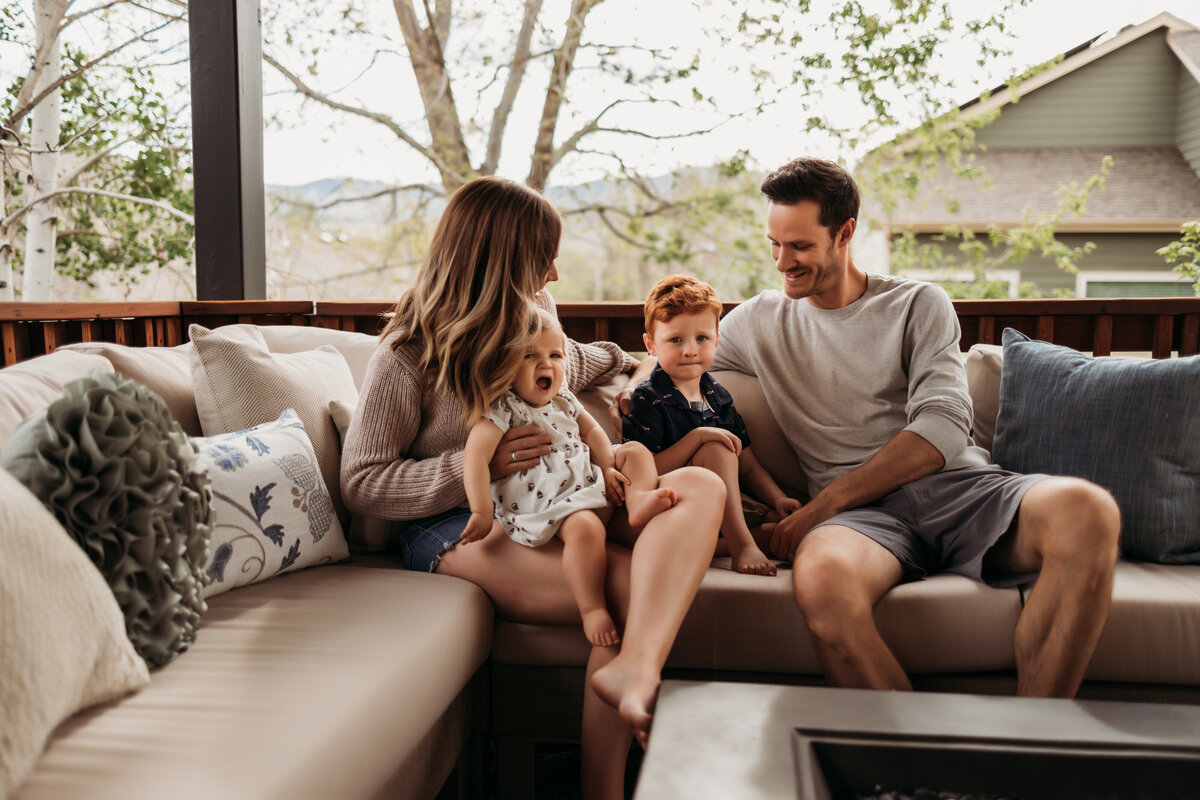 Family of four snuggle on outdoor patio furniture during a summer photo session at their home