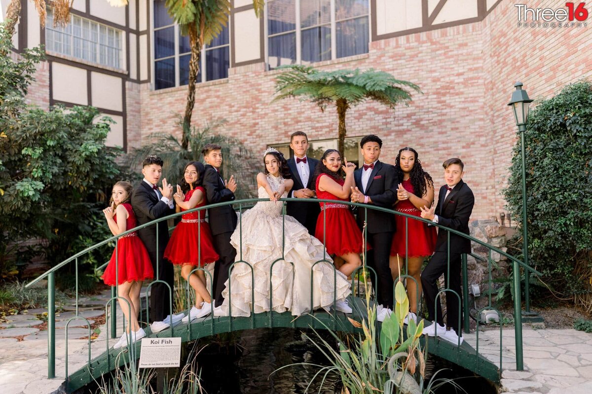 Young lady having her quinceanera poses on a bridge with young men and women honoring her