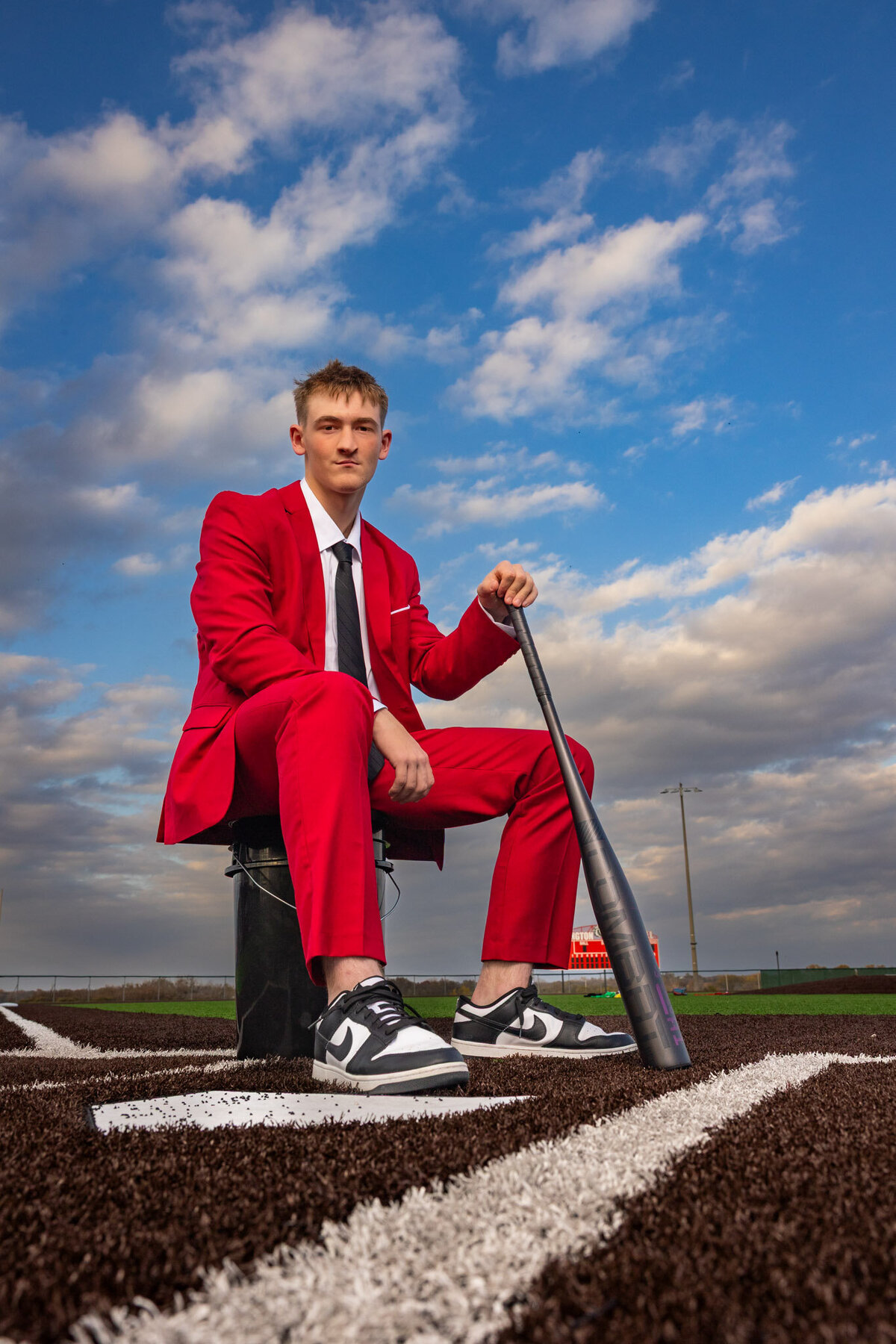 A senior guy sitting on a bucket with a bat at home plate in Lawrence, KS