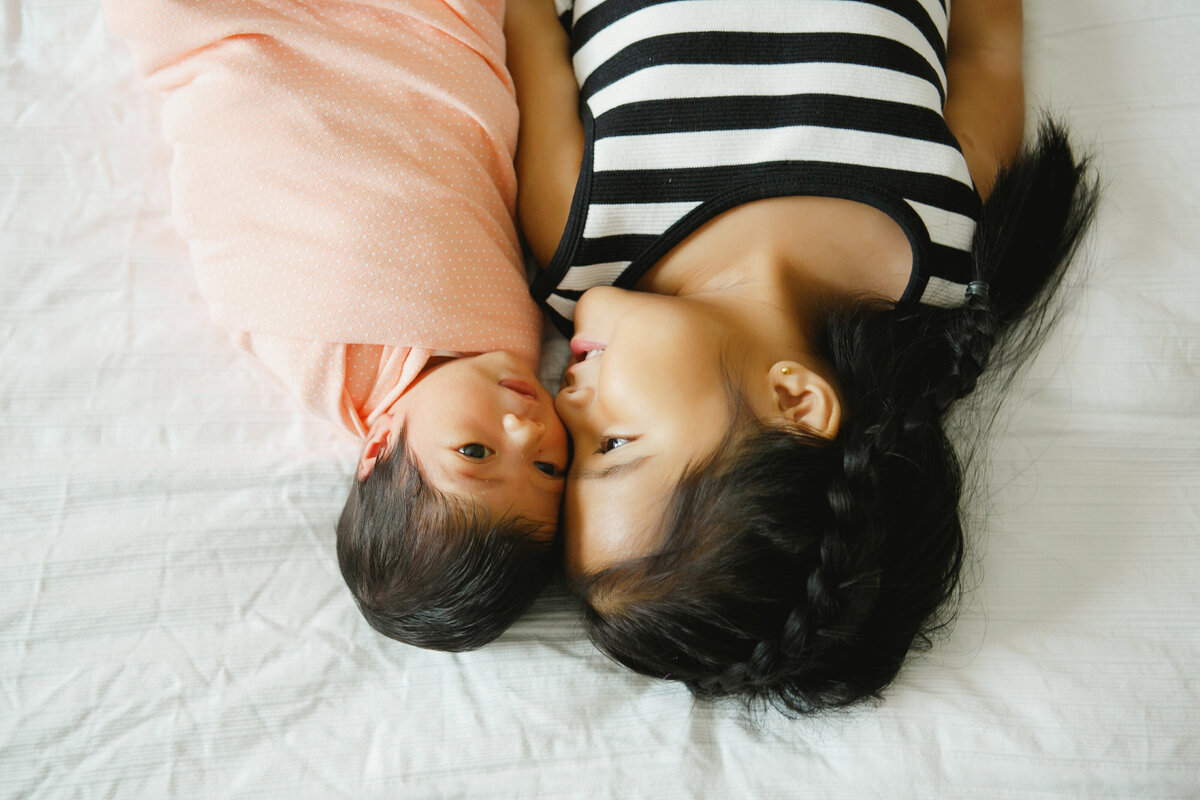 Upside portrait of bigger sister sitting with newborn touching foreheads