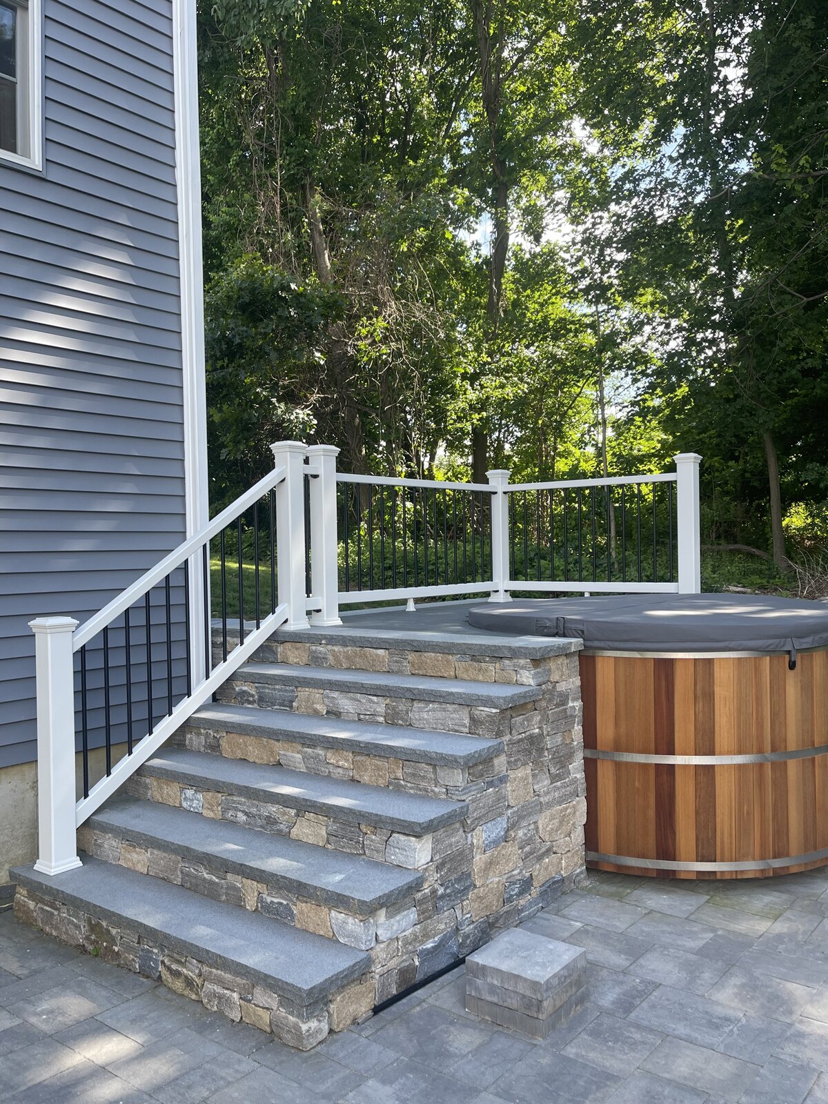 A stone set of stairs leading to a hot tub deck on a stone paved patio