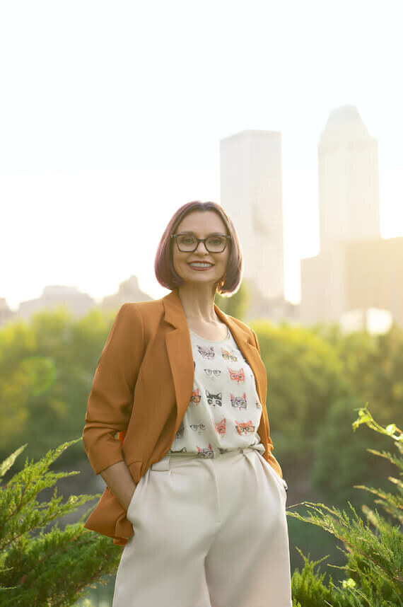 woman smiling at the camera in an orange suit with downtown tulsa skyline in the background