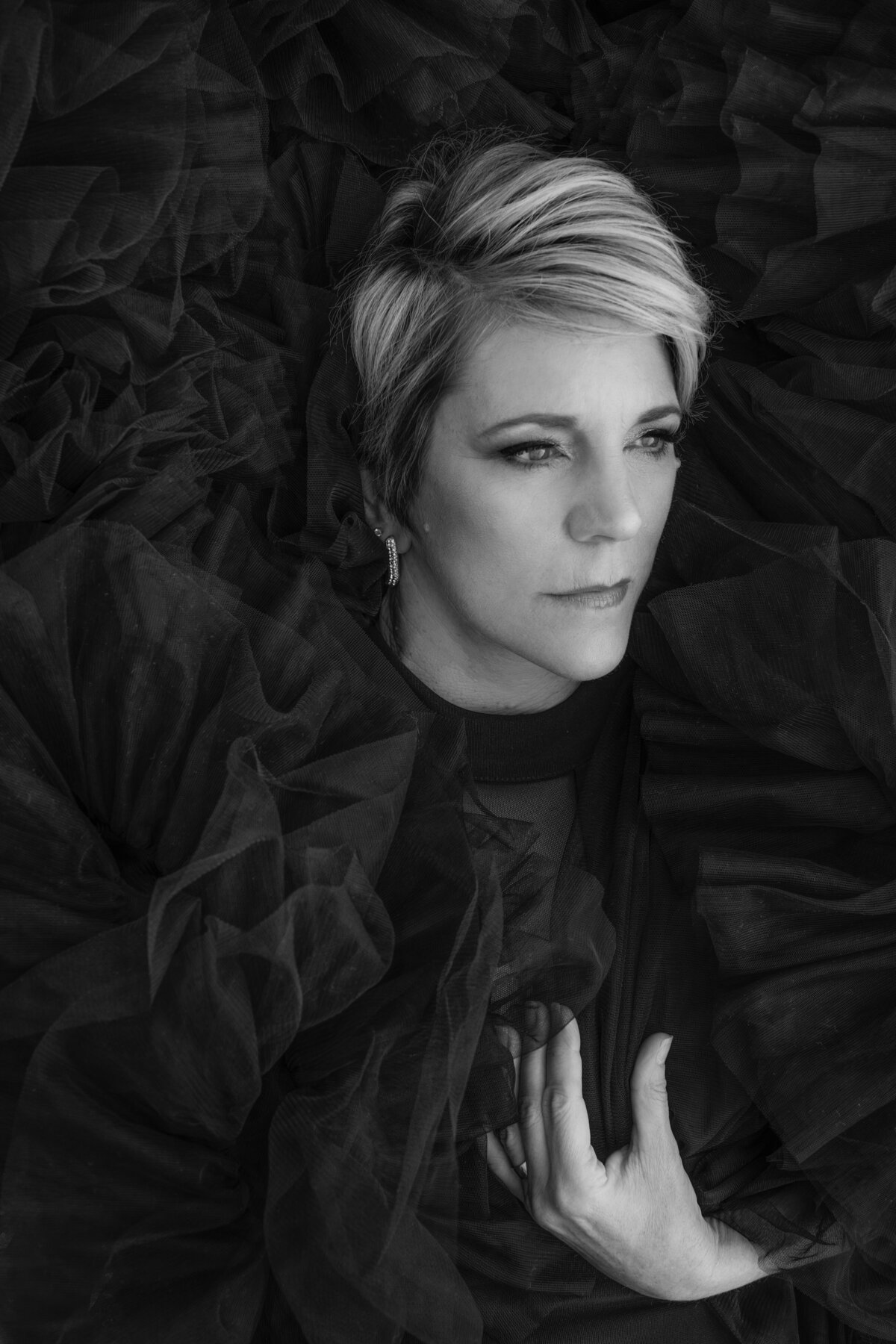 Intense black and white Cincinnati portrait featuring a woman with a sharp, short hairstyle. Surrounded by dramatic ruffled fabric, her penetrating gaze captures a deep emotion, highlighting the artistry of the shot.