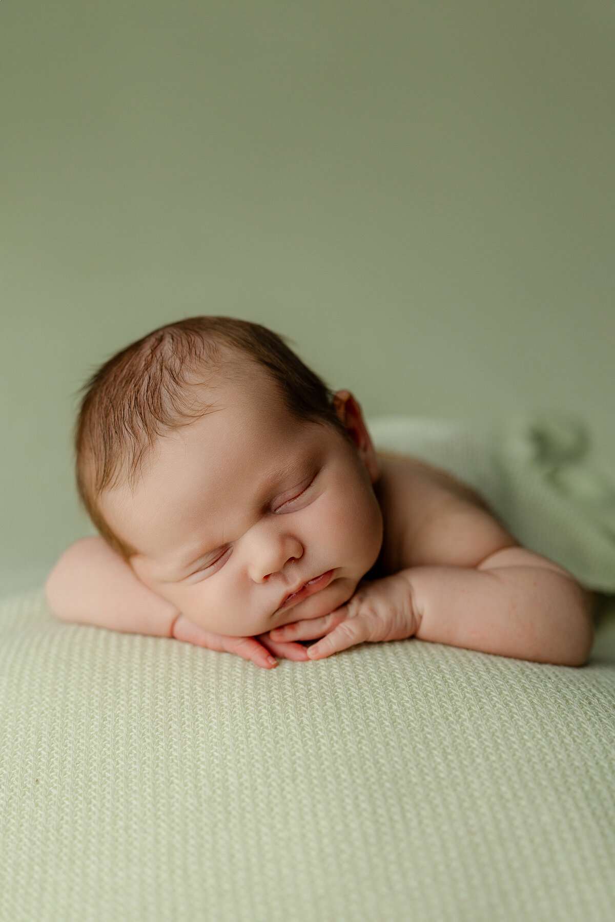 Newborn baby sleeping on a soft green knit blanket with hands tucked under chin during their studio session. Captured by Inland Empire newborn photographer Kaitlyn Dawn Photography.