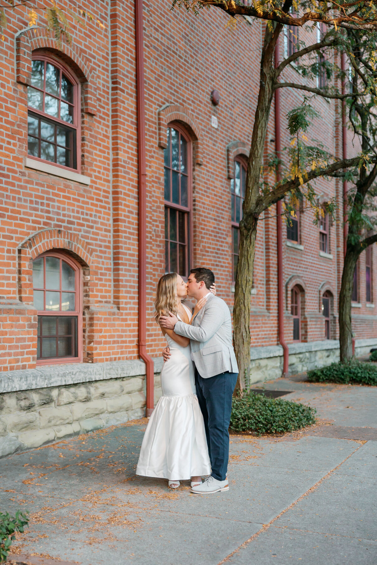 Bride and groom sharing a kiss outside a red brick building during golden hour.