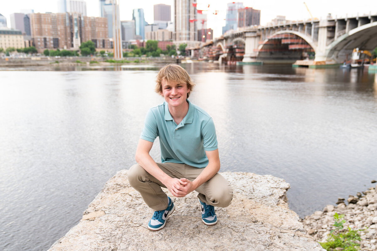 Guy poses on a rock overlooking Minneapolis, Minnesota for his senior pictures