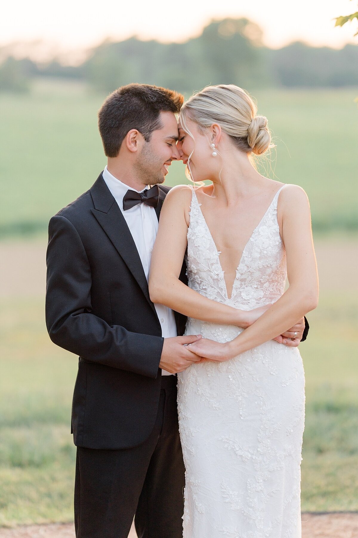sunset bridal photos with groom embracing his bride as she smiles to hime while resting her forehead on his with a setting sun in the distance illuminating the couple in a warm glow