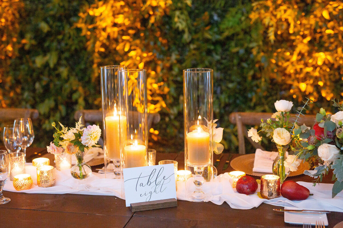 head table set for a wedding party with a green hedge wall background and gloswing candles