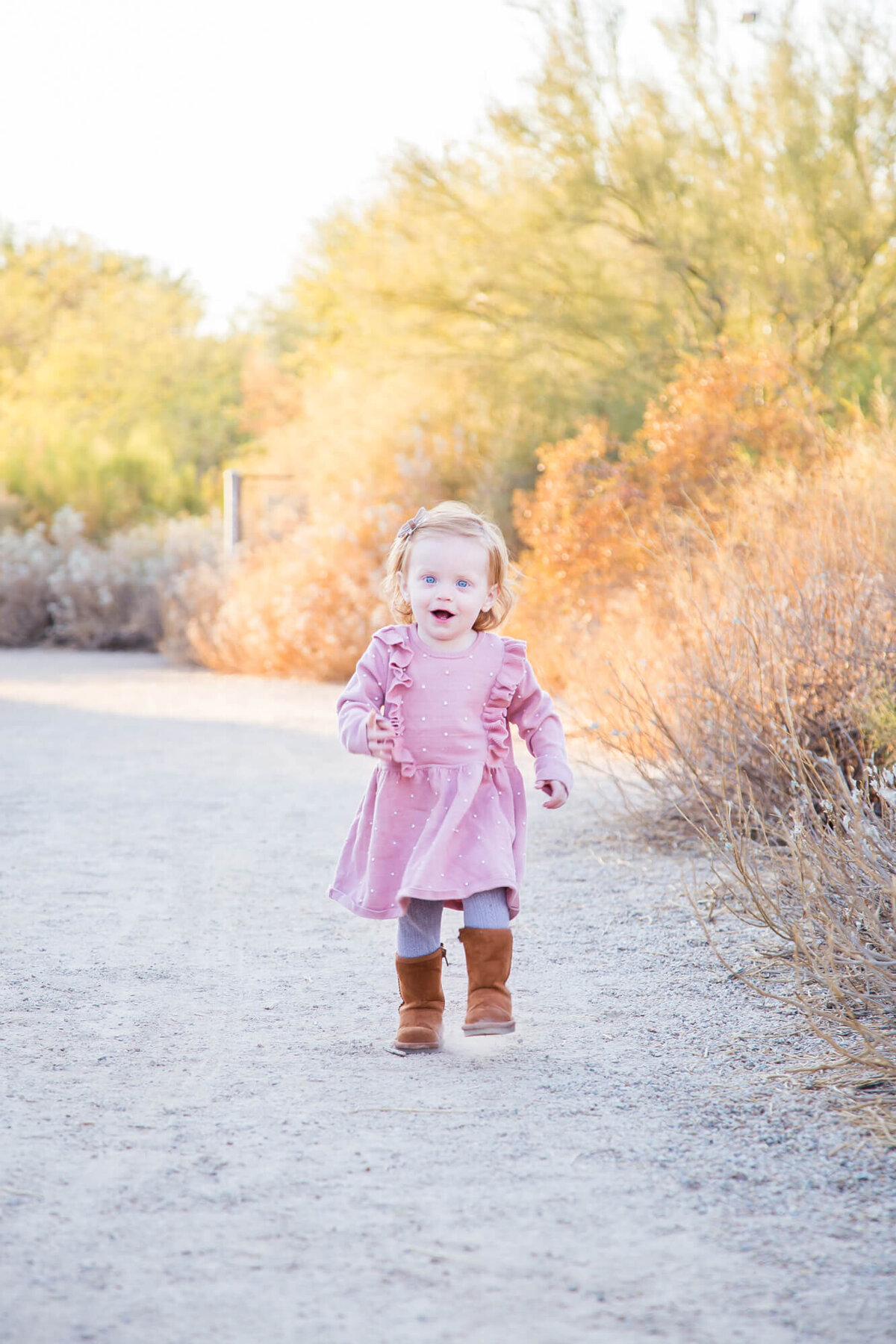 redheaded toddler girl in pink dress and boots running on a desert path