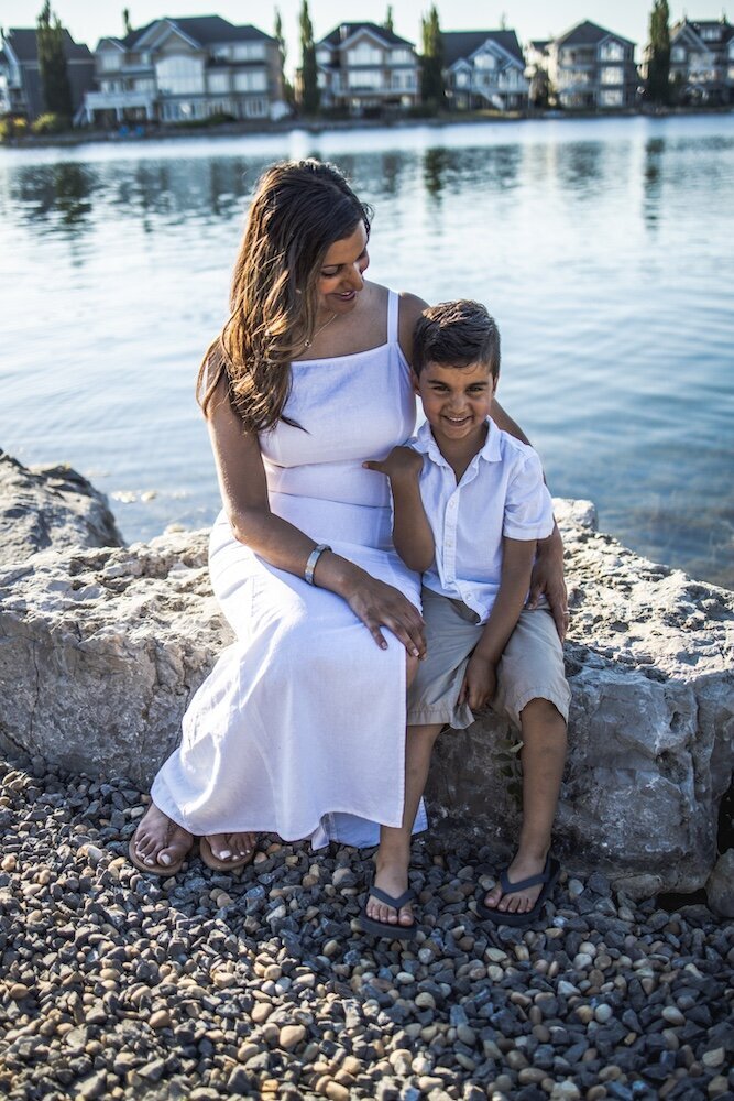Mother and son sitting side by side on a rock near a lake