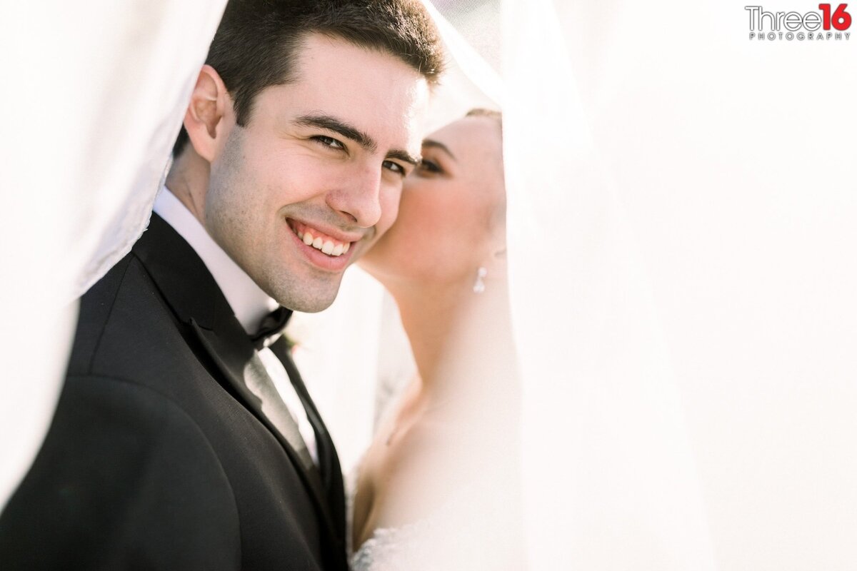 Bride whispers into her Groom's ear while they pose under her veil