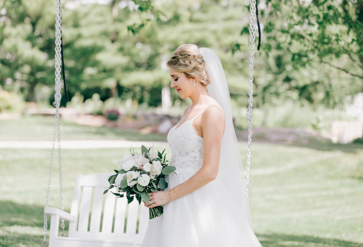 Bride looks down at luxurious bouquet of white roses and eucalyptus with gorgeous tree swing in the background