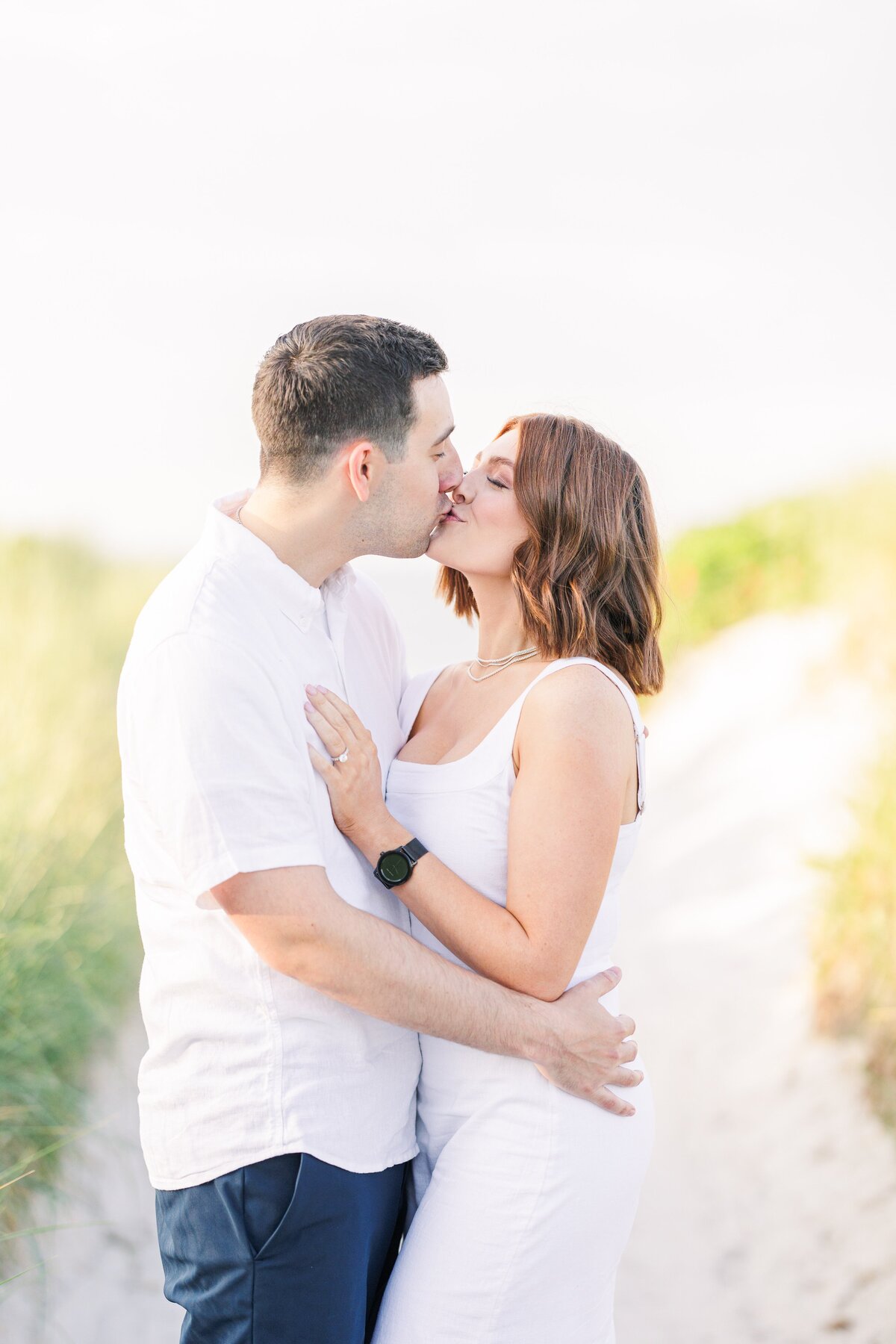A couple kissing in the sand dunes at Wingaersheek Beach during their Gloucester engagement pictures.