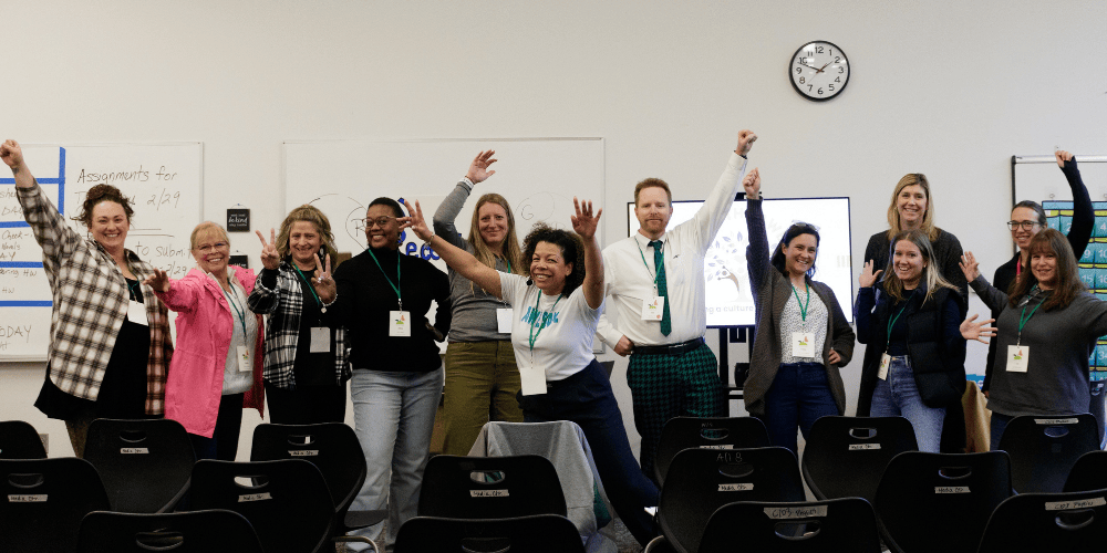 Smiling group of Activate the A.W.E.S.O.M.E. workshop participants standing in a row with arms raised in celebration, representing success, connection, and team energy after a productive session
