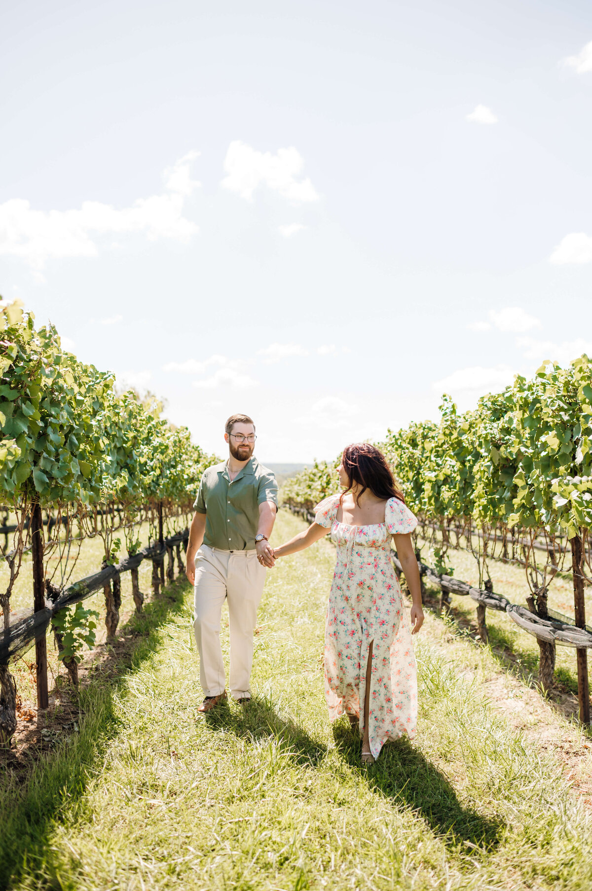 stone tower winery wedding venue with woman and man holding hands and running together down a row of lawn in between grape vines