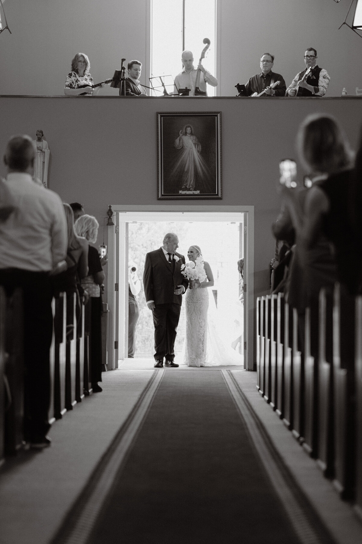 backlit father daughter as they  are about to walk down the aisle with musicians above