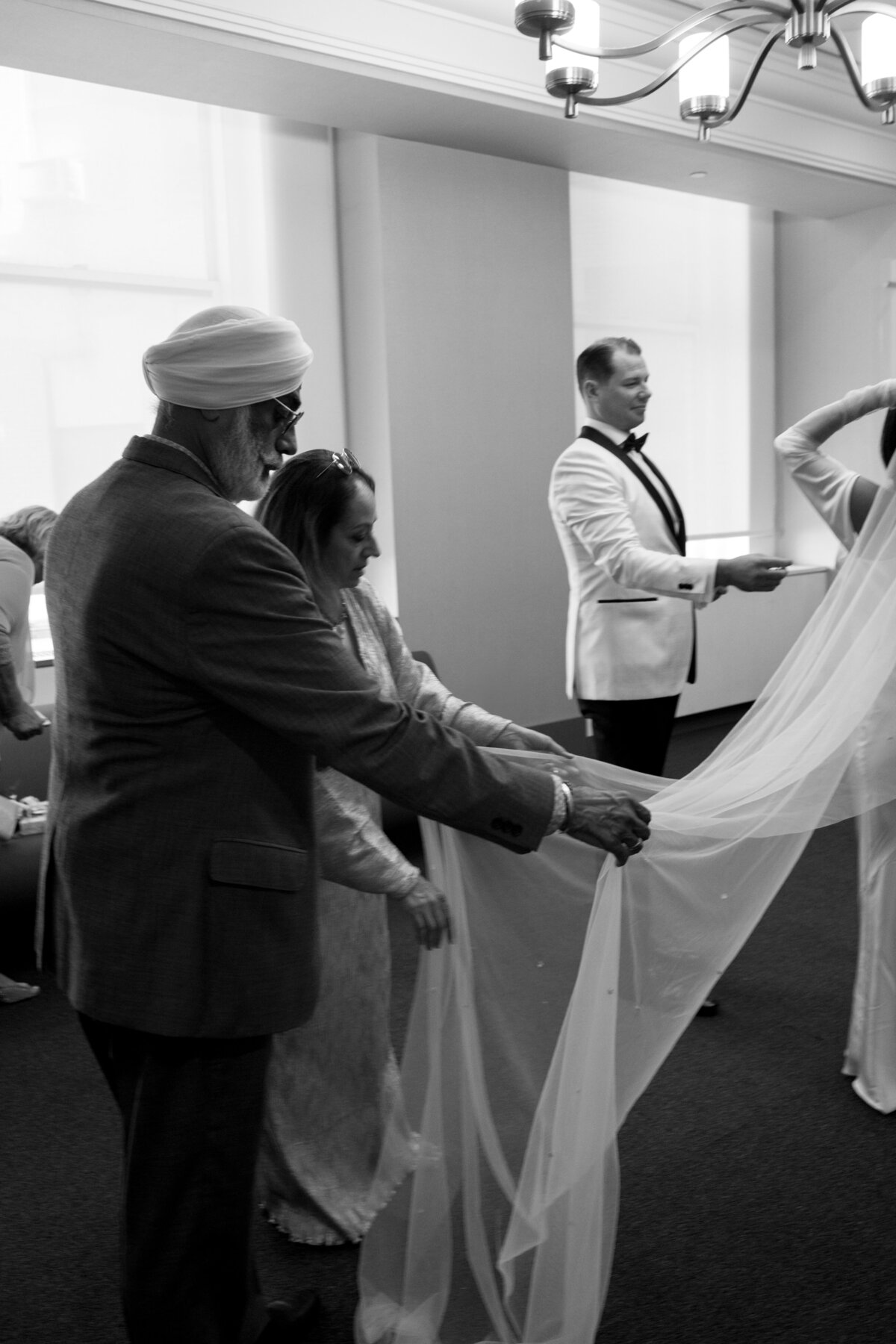 Black and white candid photo of family members adjusting the bride’s veil inside New York City Hall before the ceremony, captured during Japna and Chris’s intimate elopement by NYC wedding photographer Perry Hancock.