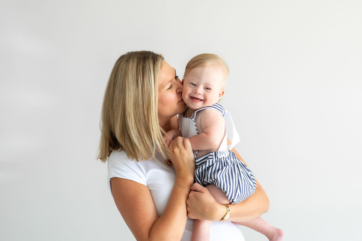 A loving mom holds her laughing toddler in her arms, gently kissing their cheek during a heartwarming moment captured in a family photo