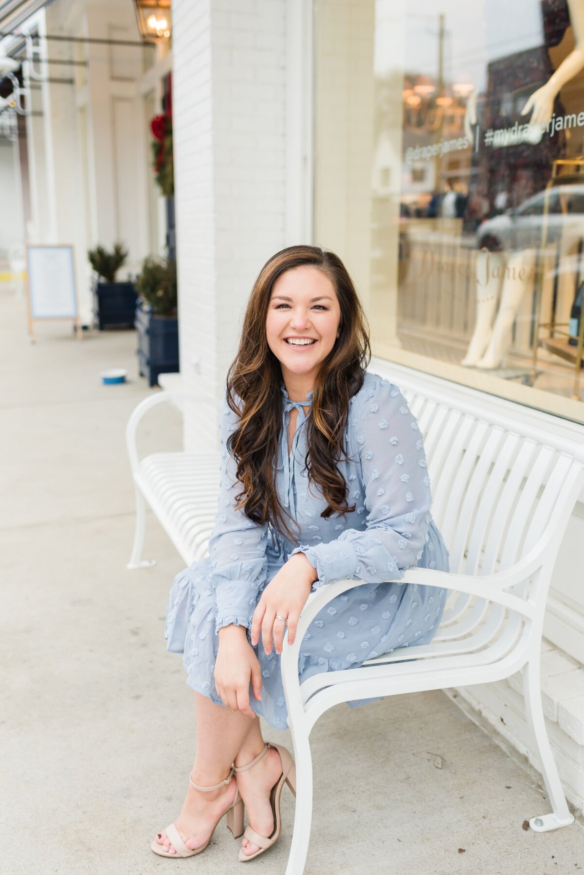 Headshot of a Nashville business owner in a blue dress sitting on a white bench outside of Draper James in 12th South
