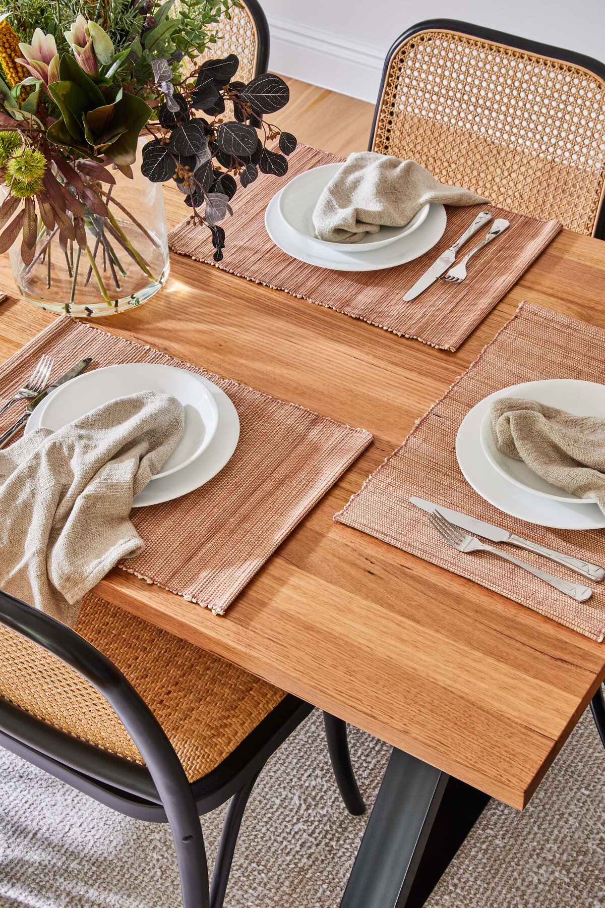 Close-up of timber dining table set with blush placemats, white plates, neutral napkins and native floral centrepiece in a Williamstown home.