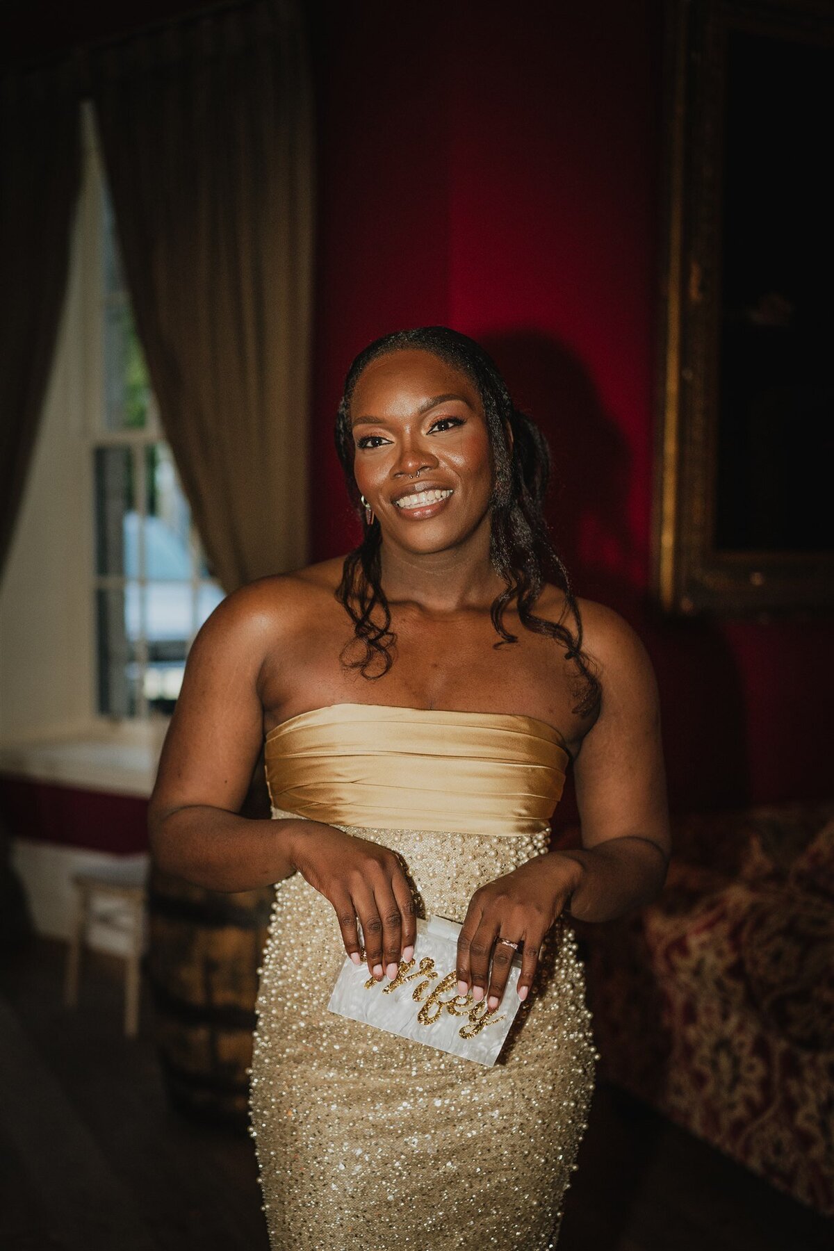 A bride wears a golden sparkly dress and poses candidly for photographs in a large living room.