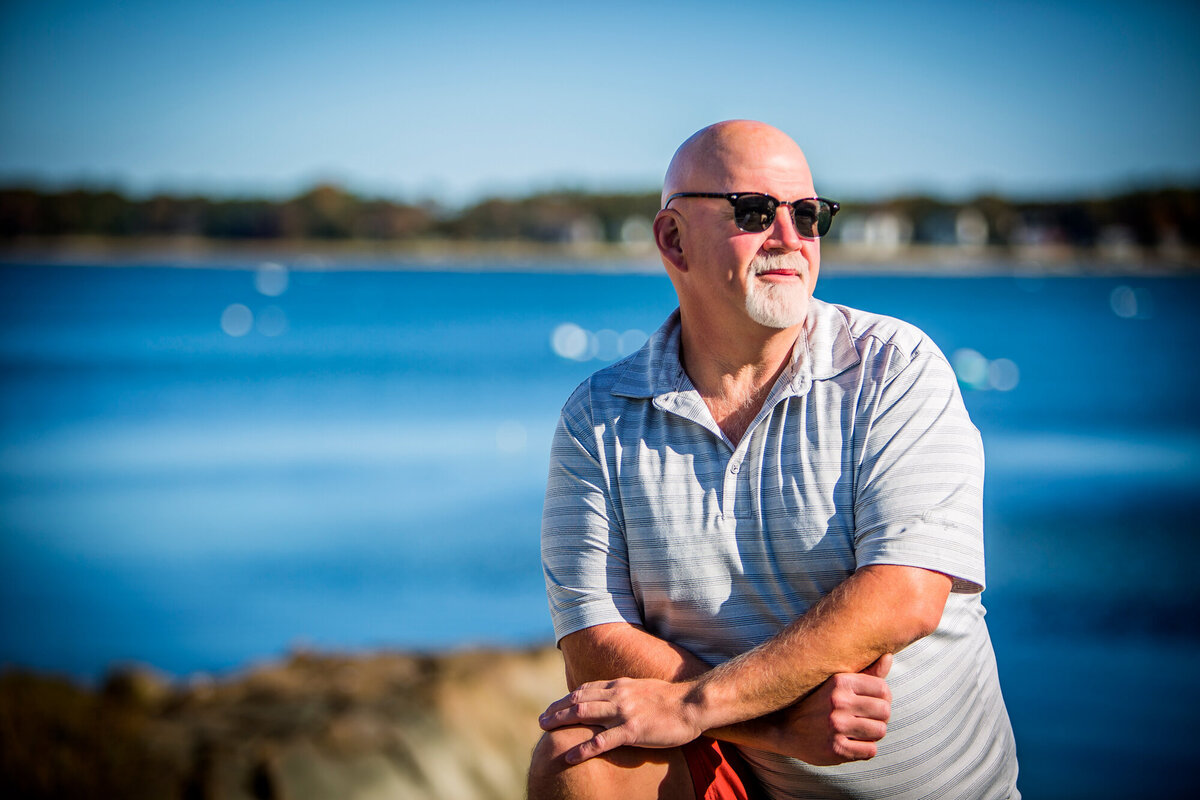 A male dating portrait client looking off in the distance with the ocean behind him