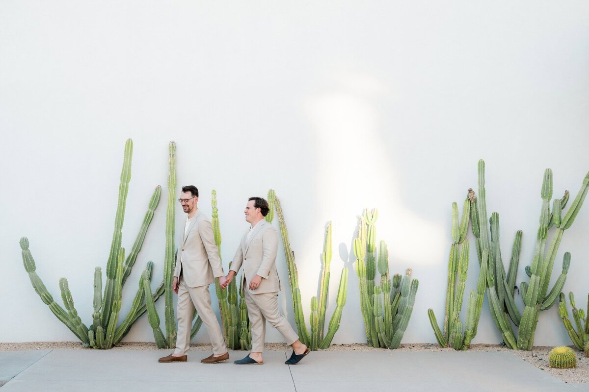 Two grooms walking in front of the cacti wall at Andaz Resort in Scottsdale holding hands