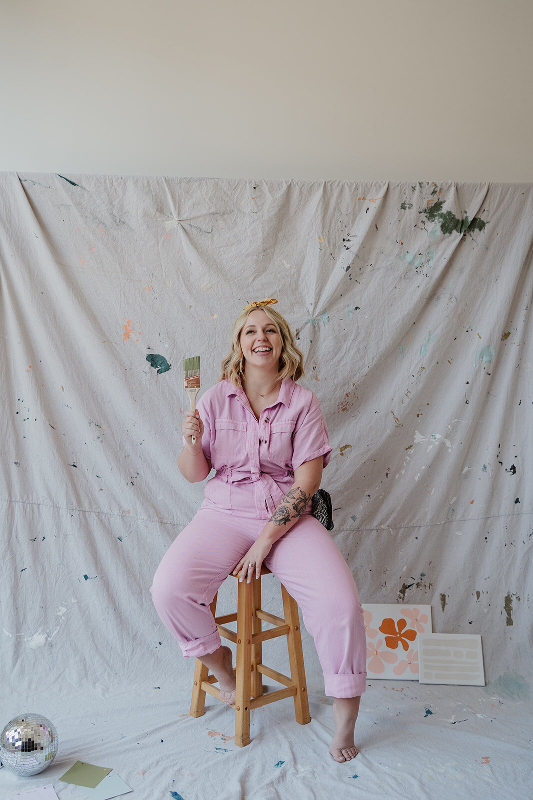 Branding portrait of a female artist sitting on a stool in a pink jumpsuit during a Wildher and Co studio session in downtown Kalamazoo Michigan.