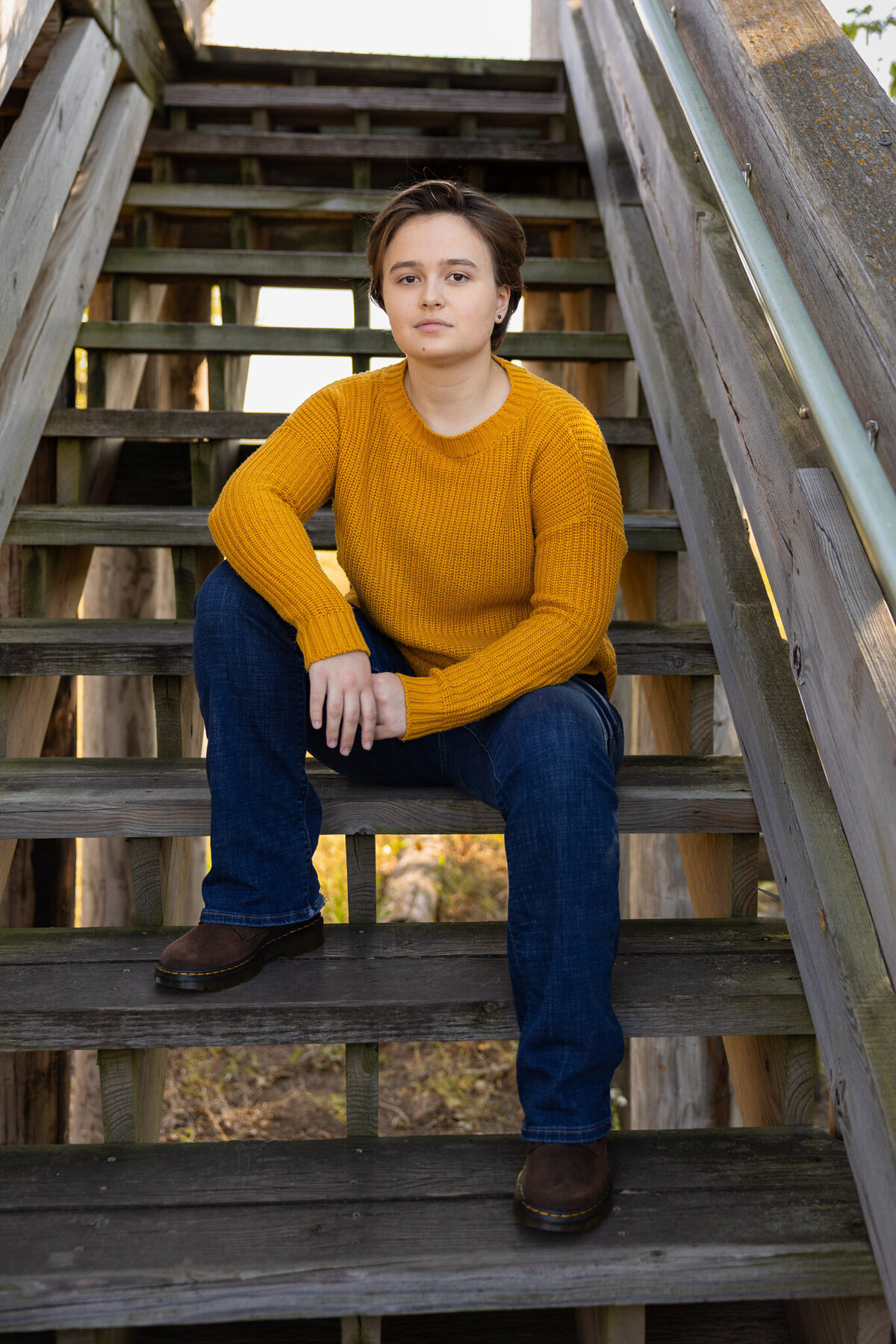 Senior girl sitting on wooden stairs wearing a mustard sweater during a senior session in Lawrence KS