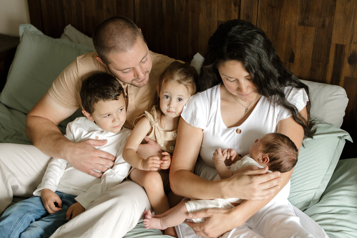 family of five sitting on bed smiling during in home lifestyle newborn session in longmont colorado