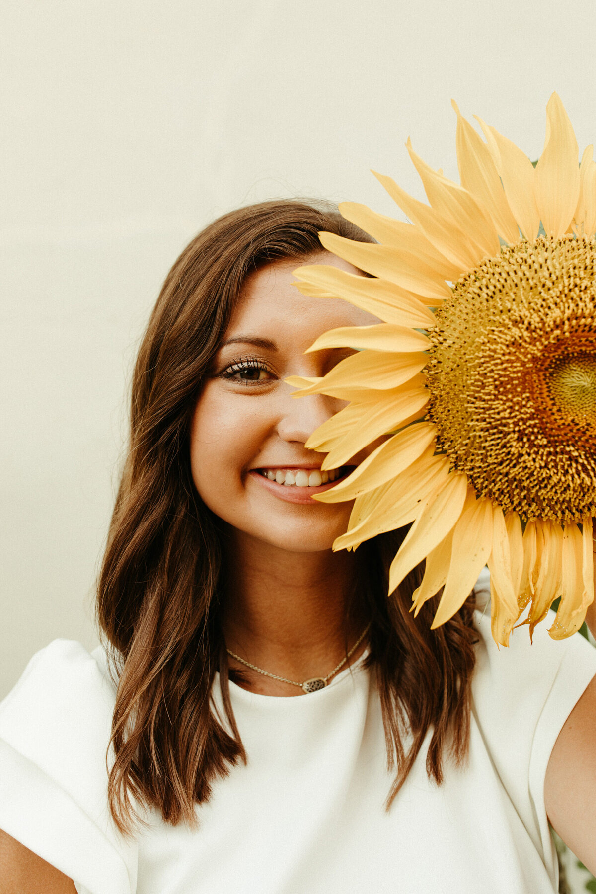 High school senior holding up a sunflower over half of her face