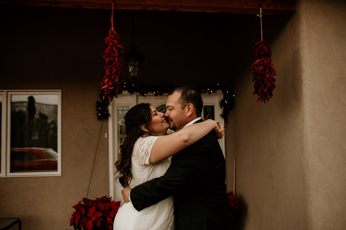 bride and groom kissing in front of adobe home