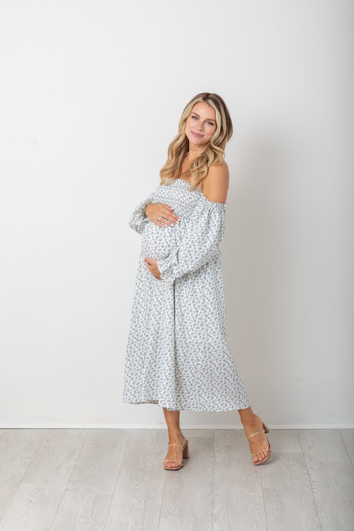 Pregnant woman in a flowing white and blue dress gently cradling her belly, captured by Philadelphia maternity photographers.