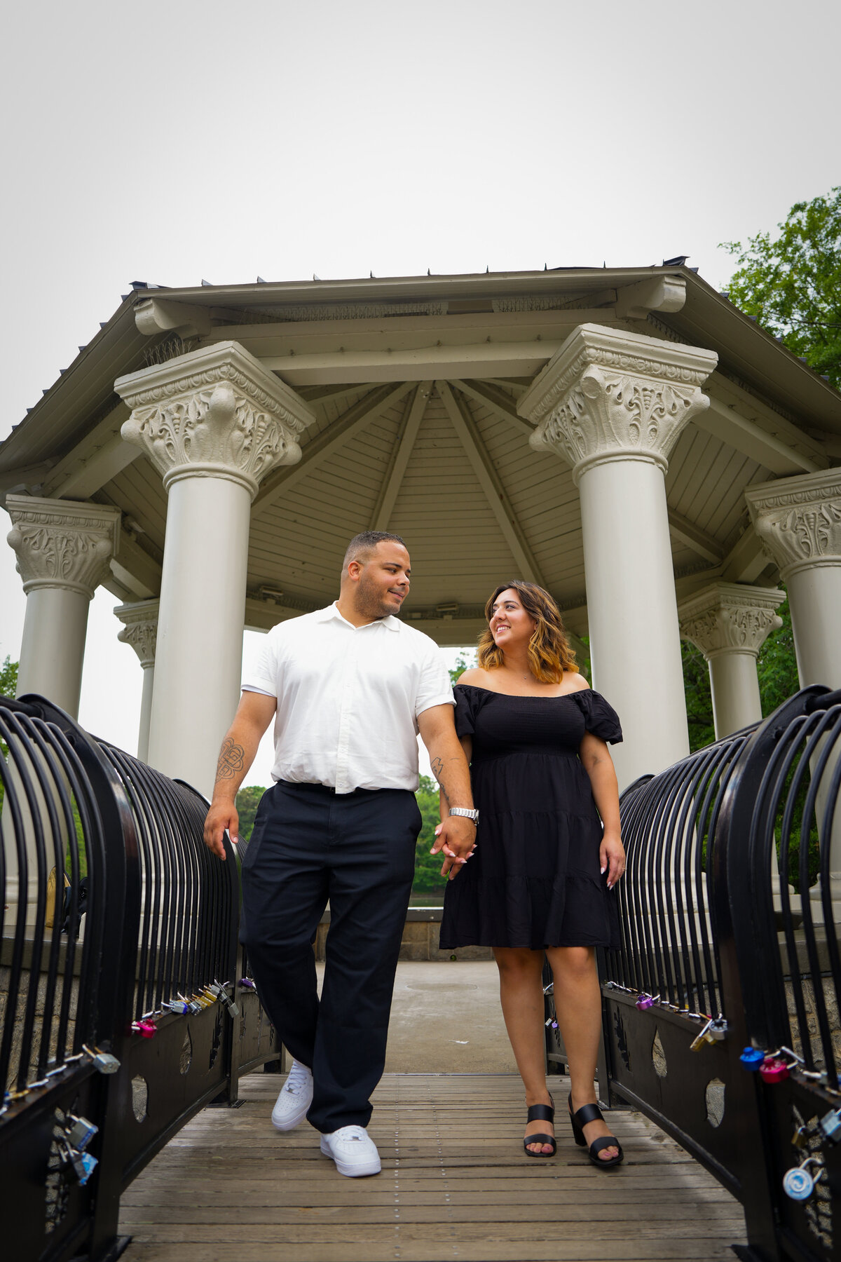 Couple walking hand-in-hand across a bridge beneath a gazebo