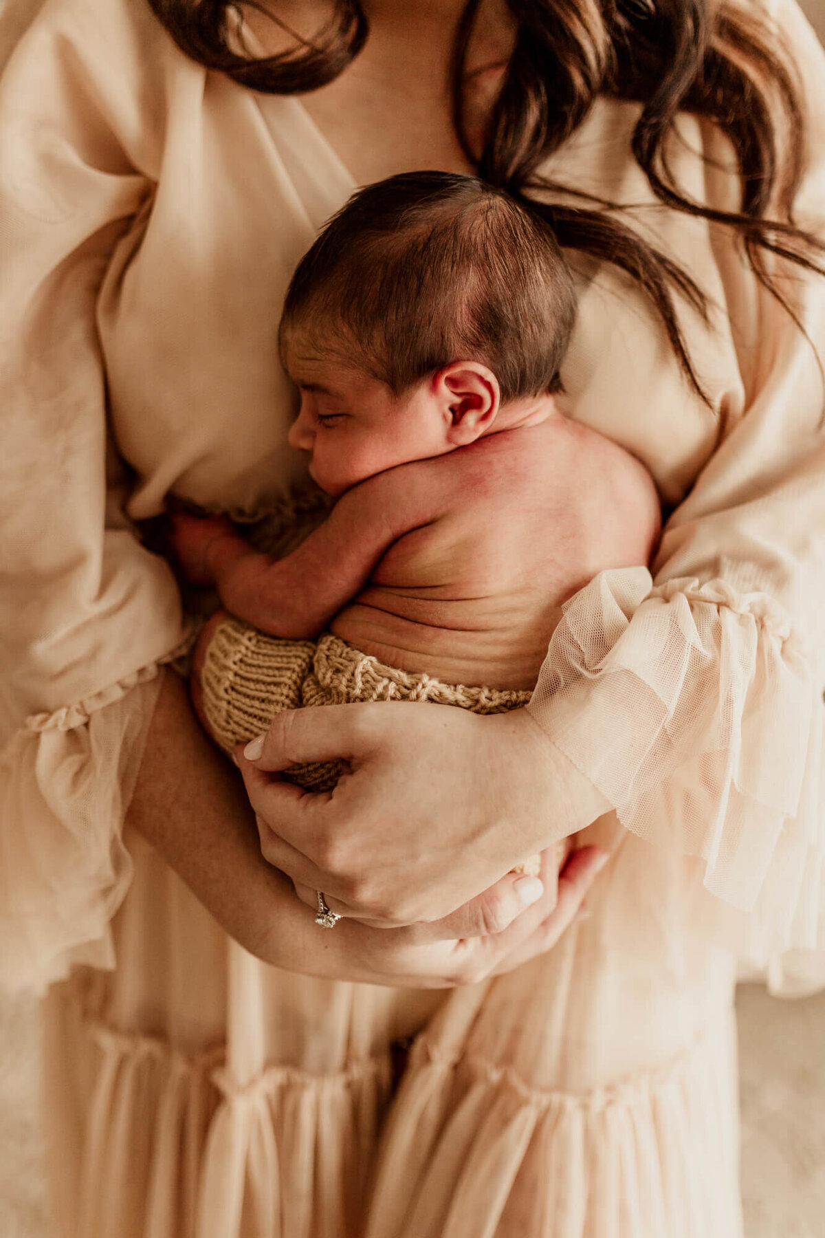 Mother wearing a brown dress holds her baby boy to her chest.