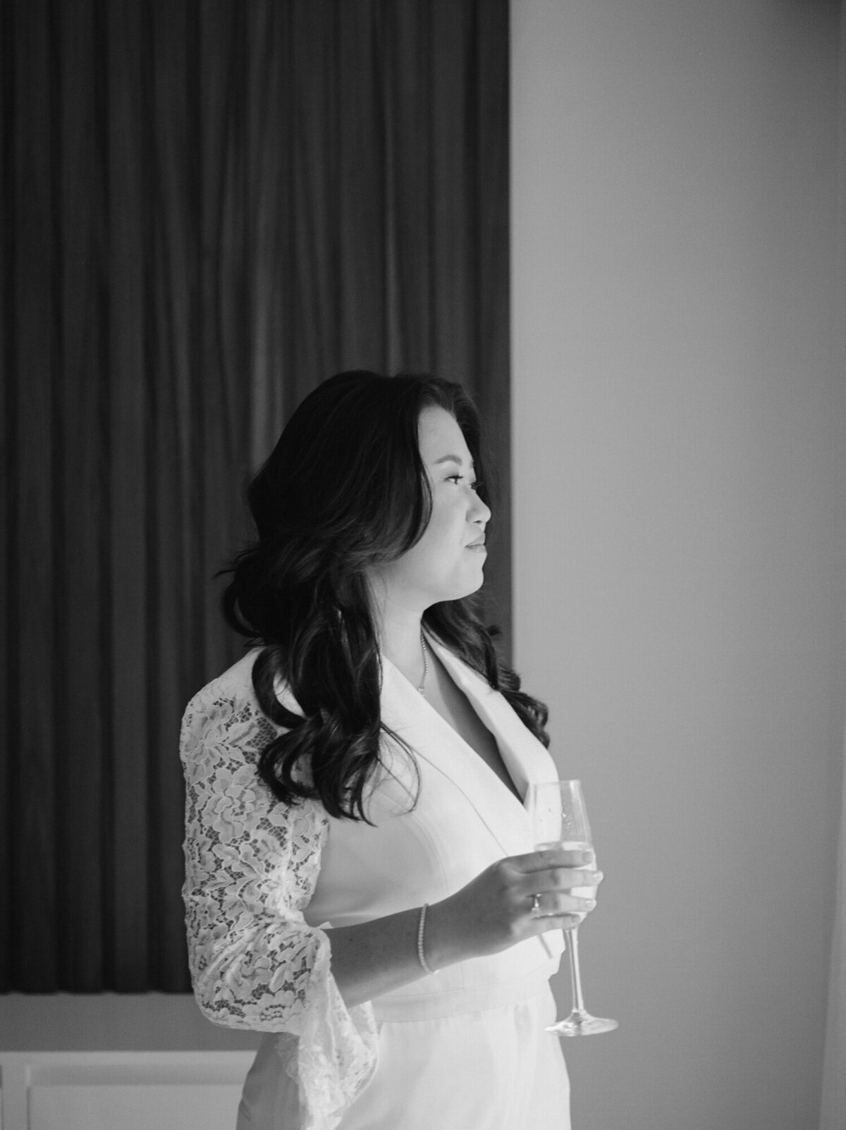 asian bride in chic pantsuit with lace sleeves sips champagne at Mexico destination wedding