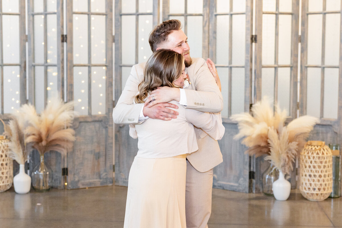 A groom tightly hugs his mother after their mother-son dance, sharing an emotional moment.