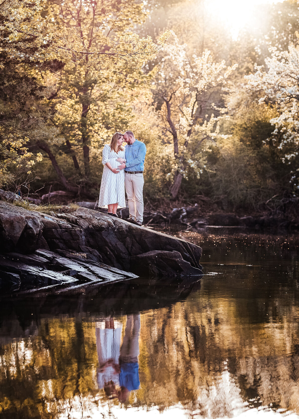 Pregnant couple on rocks, holding belly and looking into each others eyes at Carey Cottage in Portsmouth NH by Lisa Smith Photography