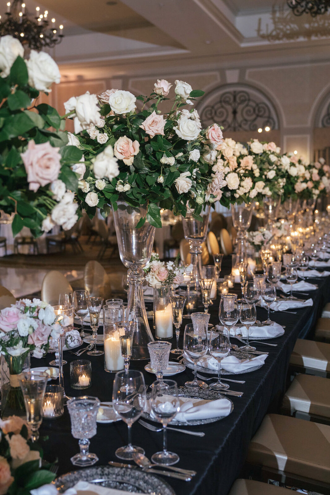 Wedding reception in the Grand Ballroom at The Adolphus Hotel featuring a long table adorned with clear glass décor, including chargers, vases, and glassware