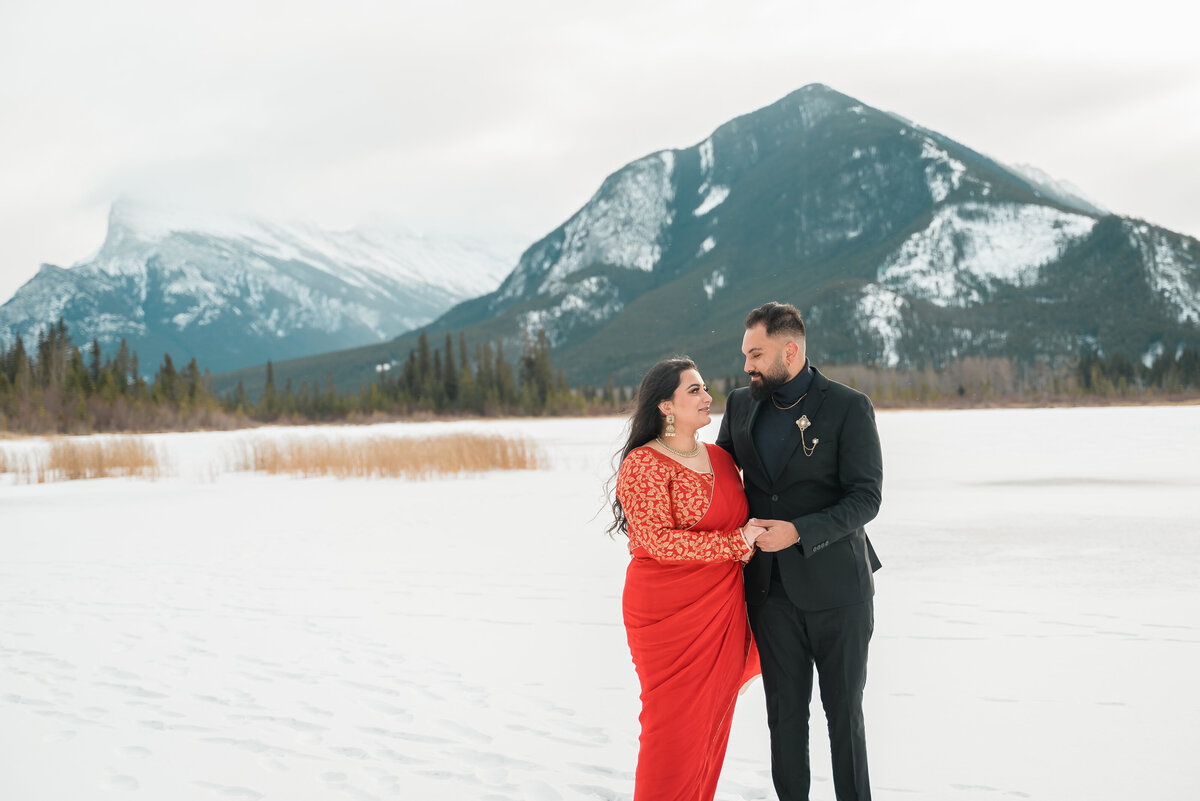 Couple standing in snowy field with Vermilion Lakes behind in Banff National Park.