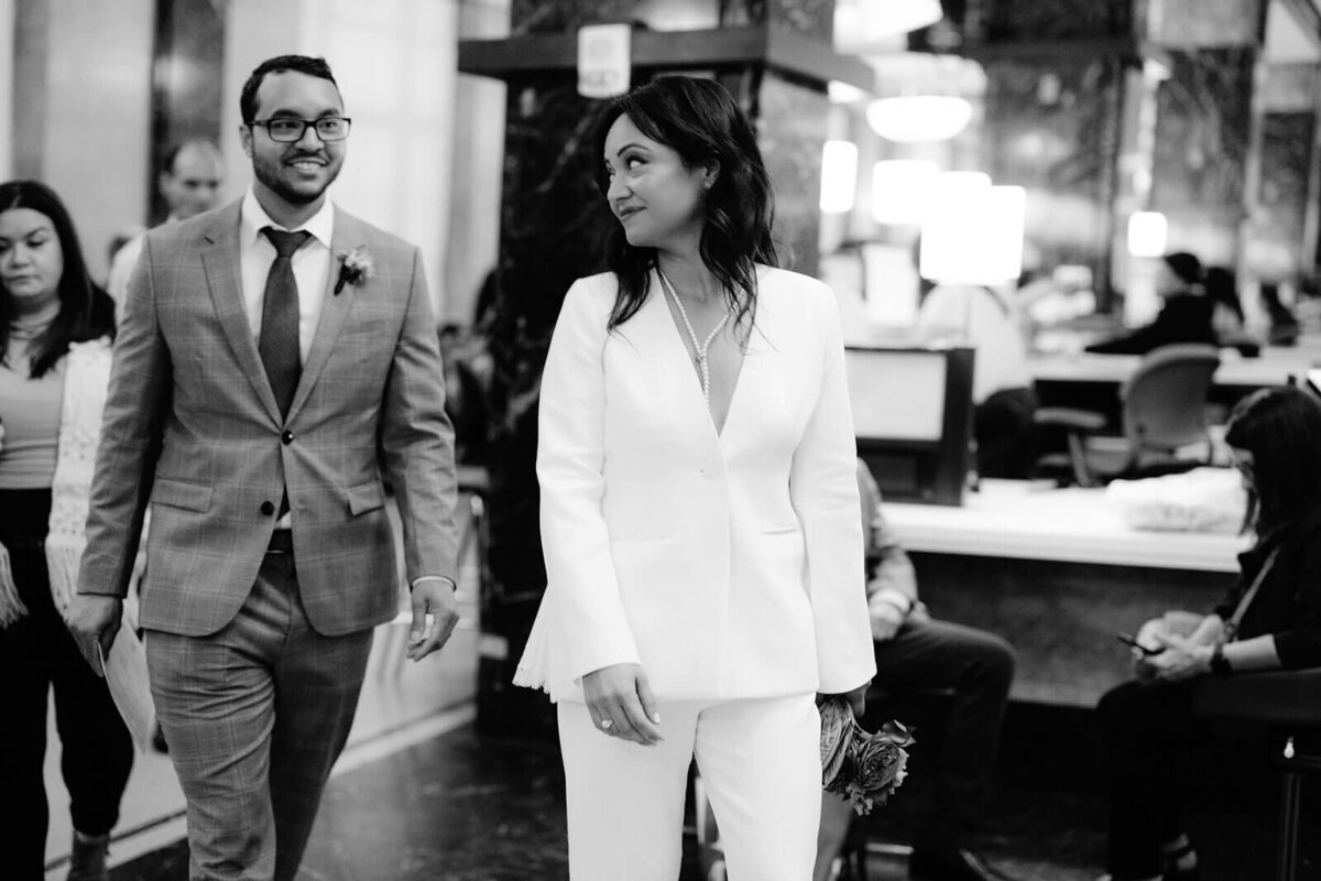 Candid shot of the bride and groom walking inside New York City Hall. Image by Jenny Fu Studio