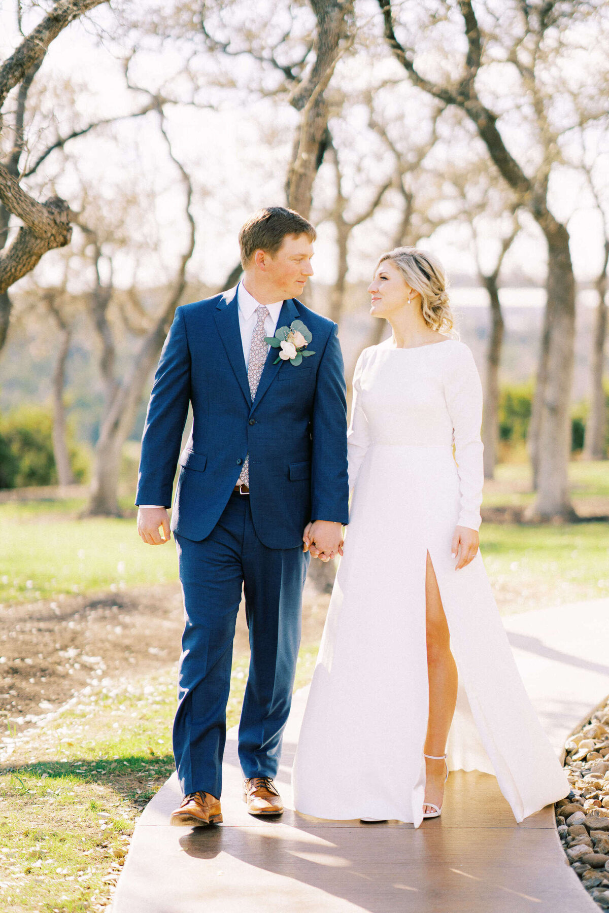 Sweet moment with newly married husband and wife walking through trees in Dripping Springs, Texas