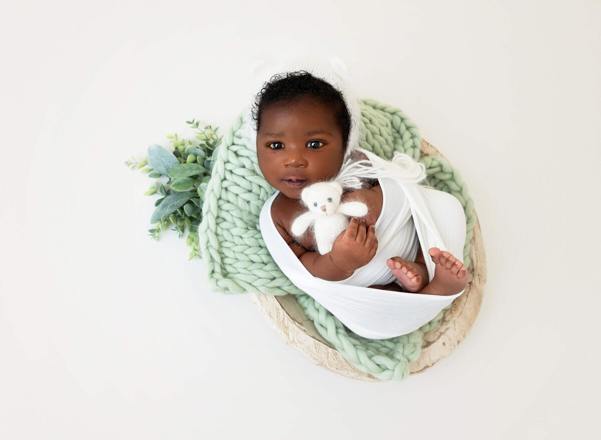 Baby boy black wrapped in white  and laying on a  sage blanket 