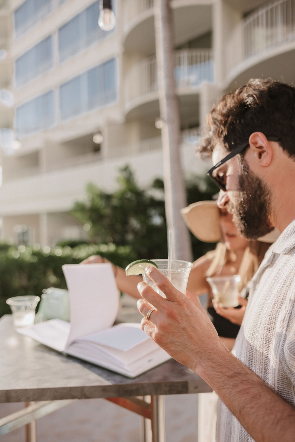 man holding drink looking at open book with the sun shining