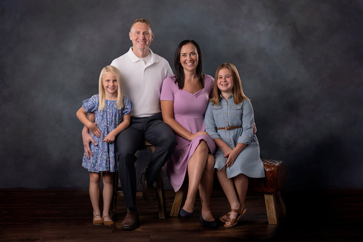 Family of 4 sit next to each other on a neutral grey background