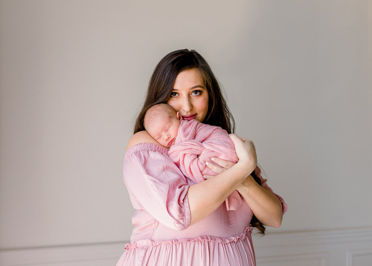 Momma in pink long, flowy dress in white studio holding swaddled baby in pink. Image captured by Brandon, Mississippi photographer.