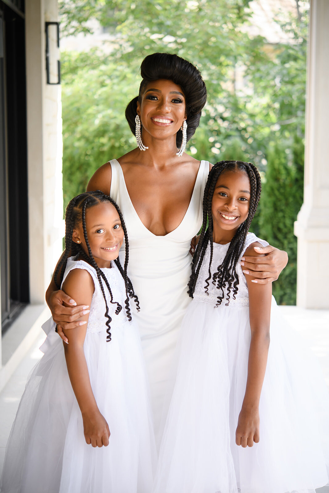 The bride stands with two young girls in matching white dresses, radiating joy.